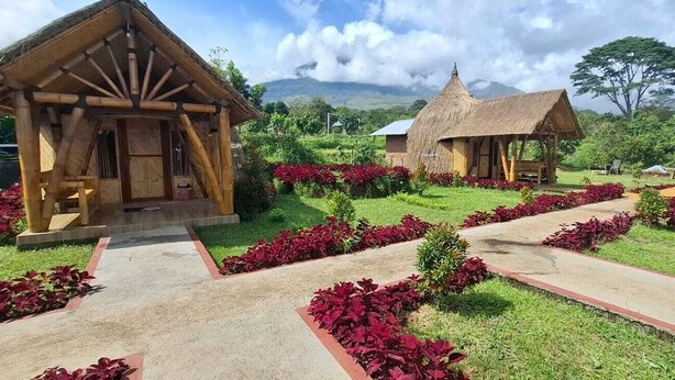 A rustic lodge with thatched-roof cabins, surrounded by well-maintained gardens and a mountainous backdrop. - Bale Gantar (Sembalun Lawang)