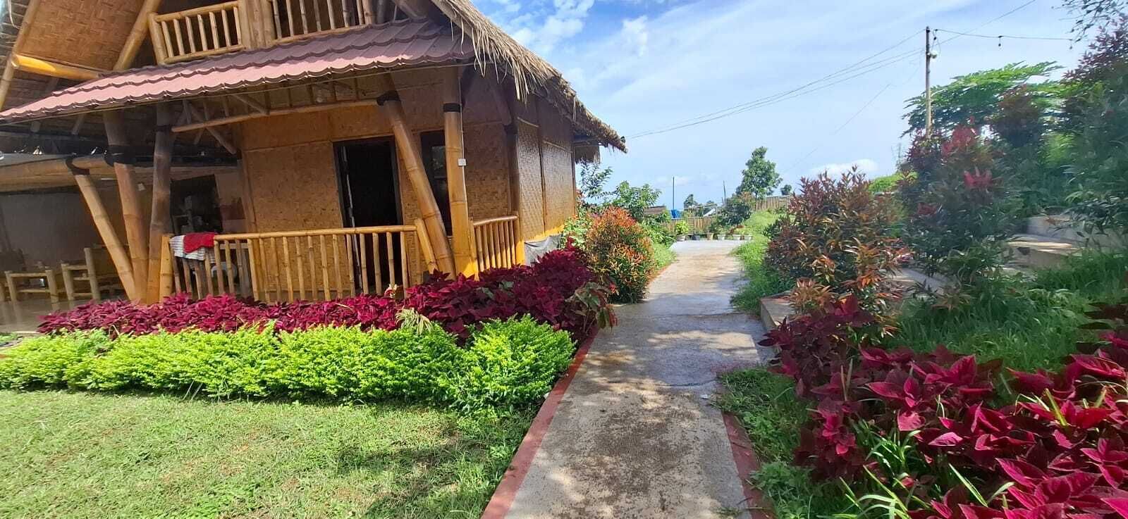 A wooden house with a porch, surrounded by well-maintained gardens and a clear pathway leading to the entrance.