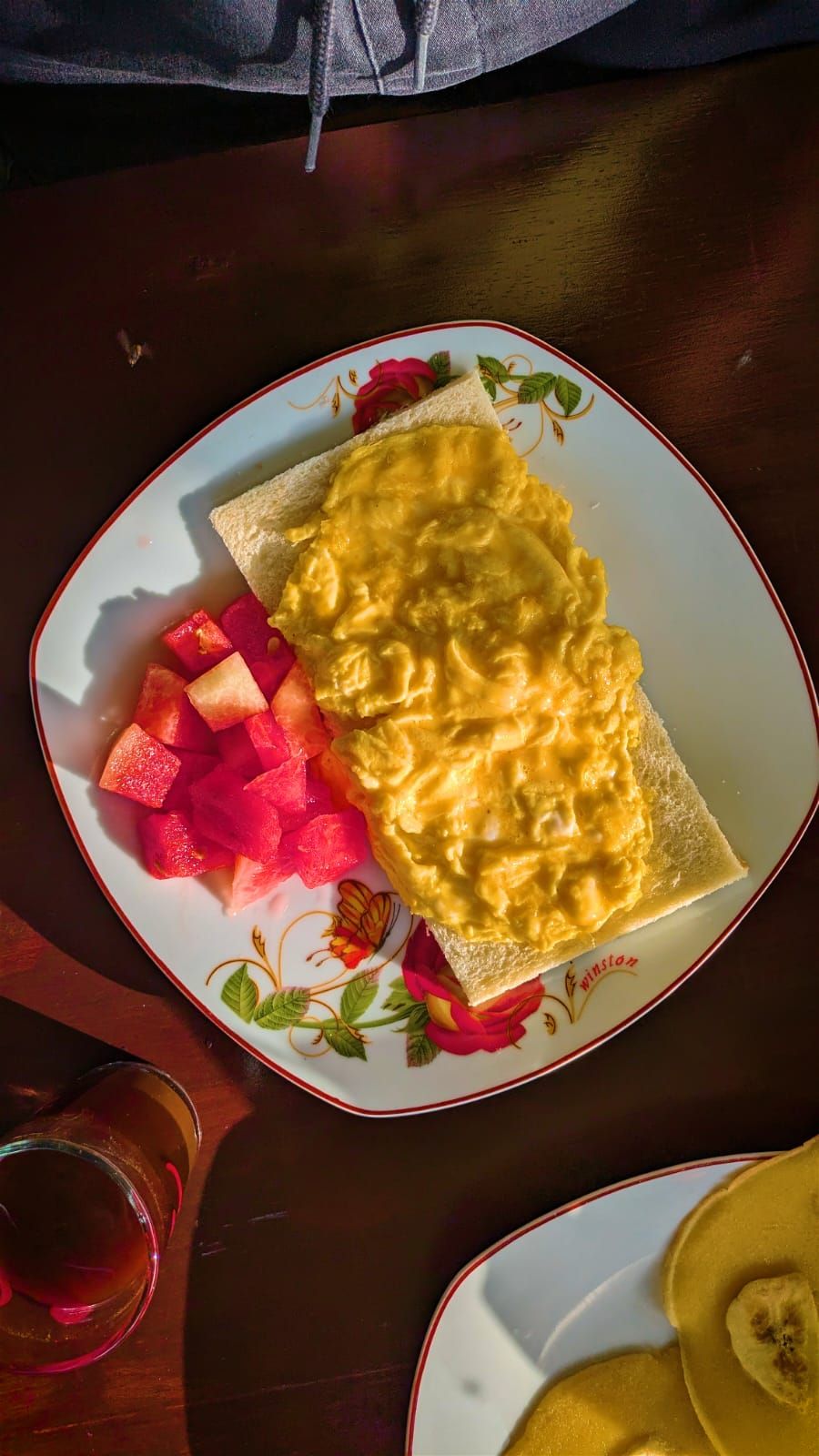 A plate with a crepe, diced watermelon, and a glass of red beverage on a wooden table.