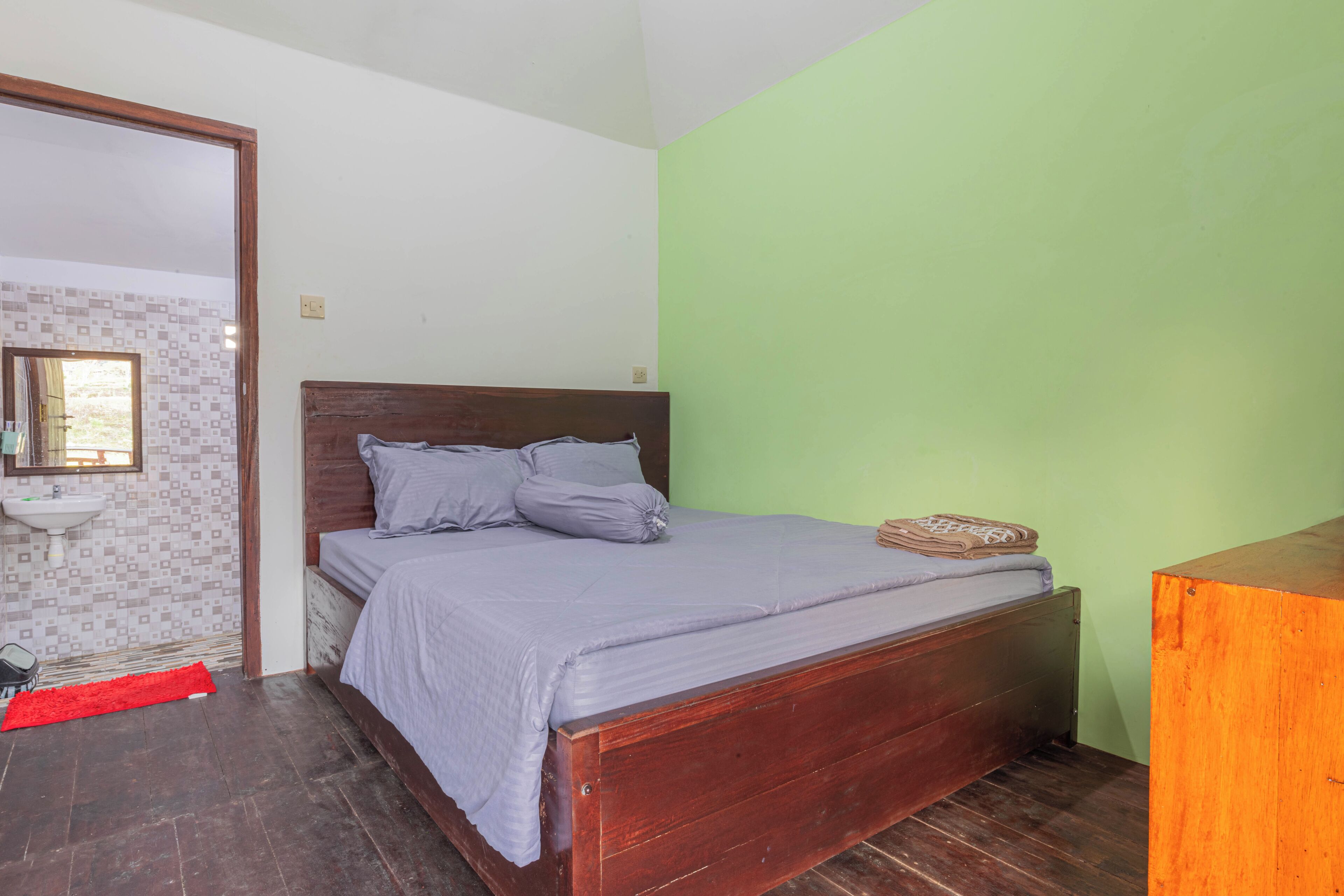 A bedroom with a wooden bed, a red rug, a sink, and a green wall.