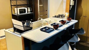A modern kitchen with a central island, bar stools, a microwave, and a gas stove. - Matsuyamachi Dotonbori Condo (Osaka)