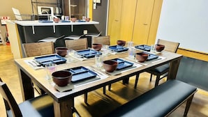 A dining area with a long table set for multiple people, equipped with plates, bowls, and glasses. - Matsuyamachi Dotonbori Condo (Osaka)
