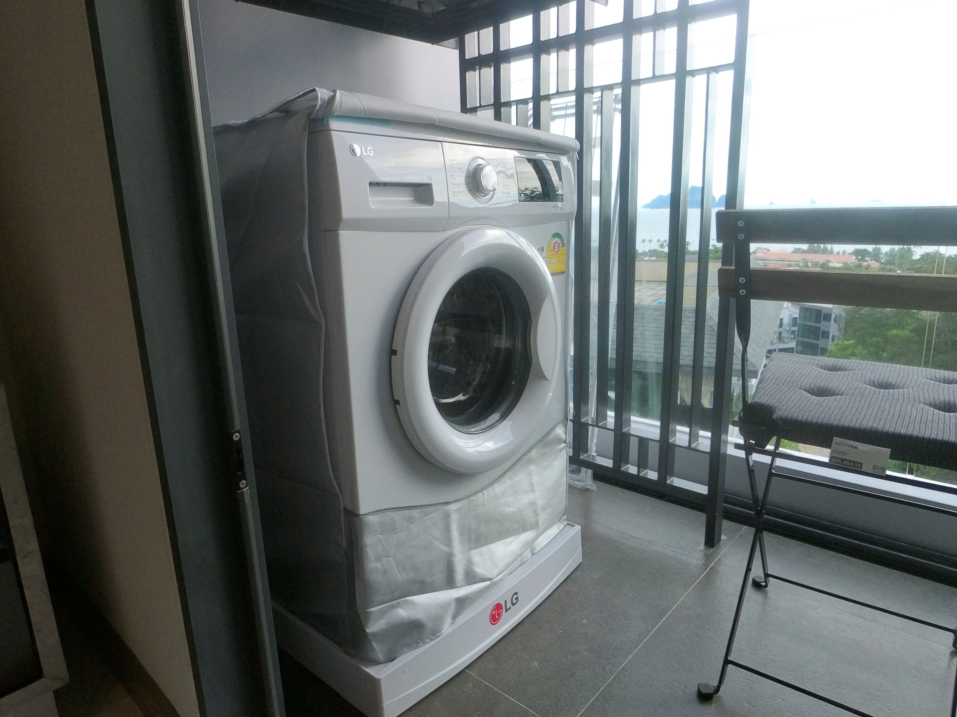 Un lave-linge LG à chargement frontal se trouve dans une pièce dotée d’une grande fenêtre, d’une étagère en métal et offrant une vue sur le paysage urbain.