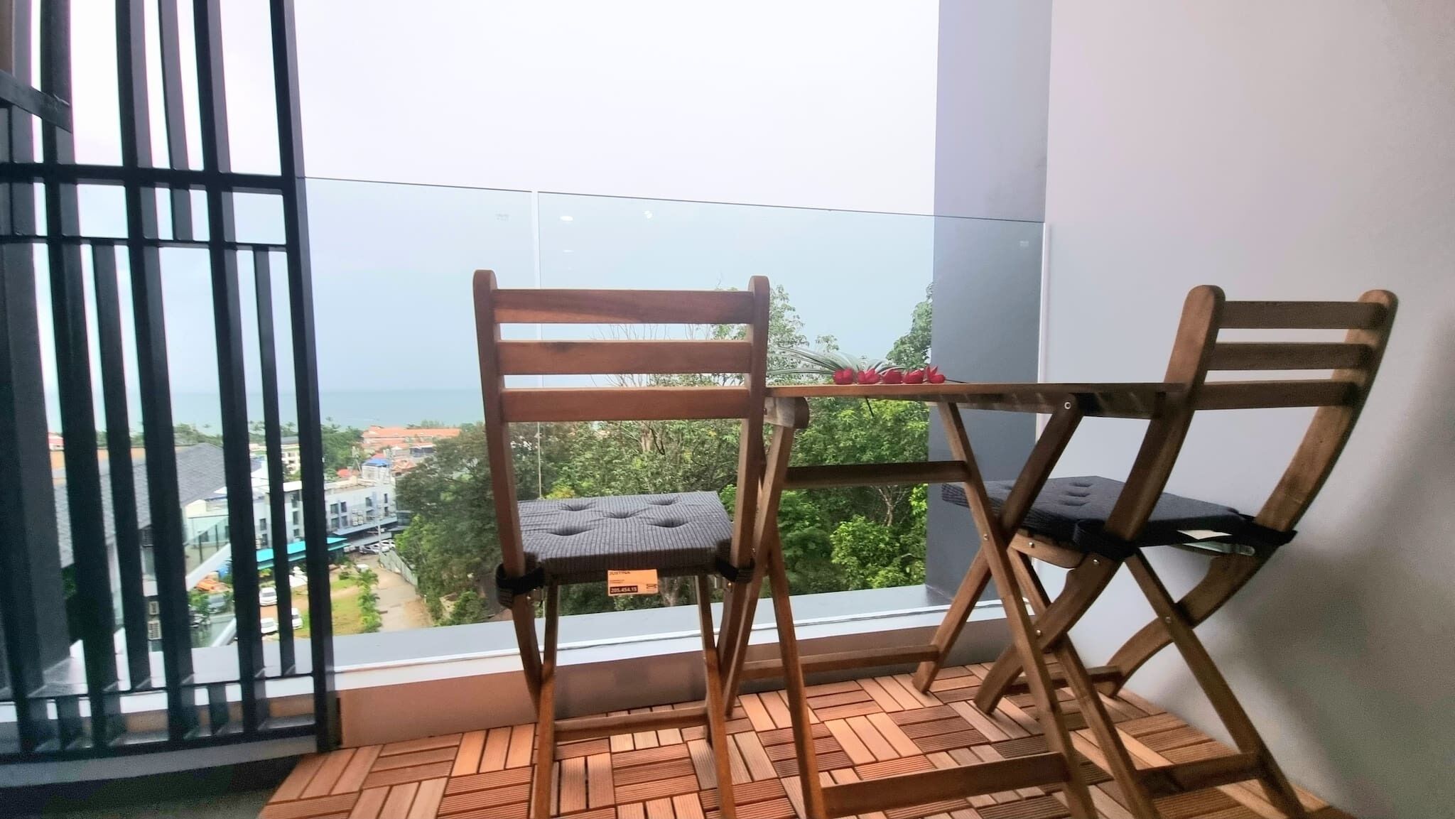 Un balcon avec deux chaises en bois et une petite table, donnant sur un paysage urbain avec des bâtiments et de la verdure.
