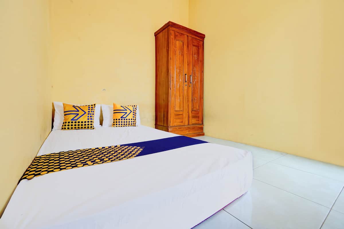 Un lit bien fait, avec une couvre-lit à motifs et des oreillers, une armoire en bois et un mur jaune uni.
