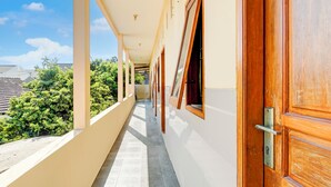 A corridor with a wooden door, windows, and a view of greenery and buildings. - OYO Life 93290 Homestay Betro Syariah (Sidoarjo)