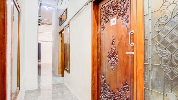 A hallway with a wooden door featuring intricate carvings and a number plate, leading to a room with a tiled floor and a decorative glass door. - OYO Life 93290 Homestay Betro Syariah (Sidoarjo)
