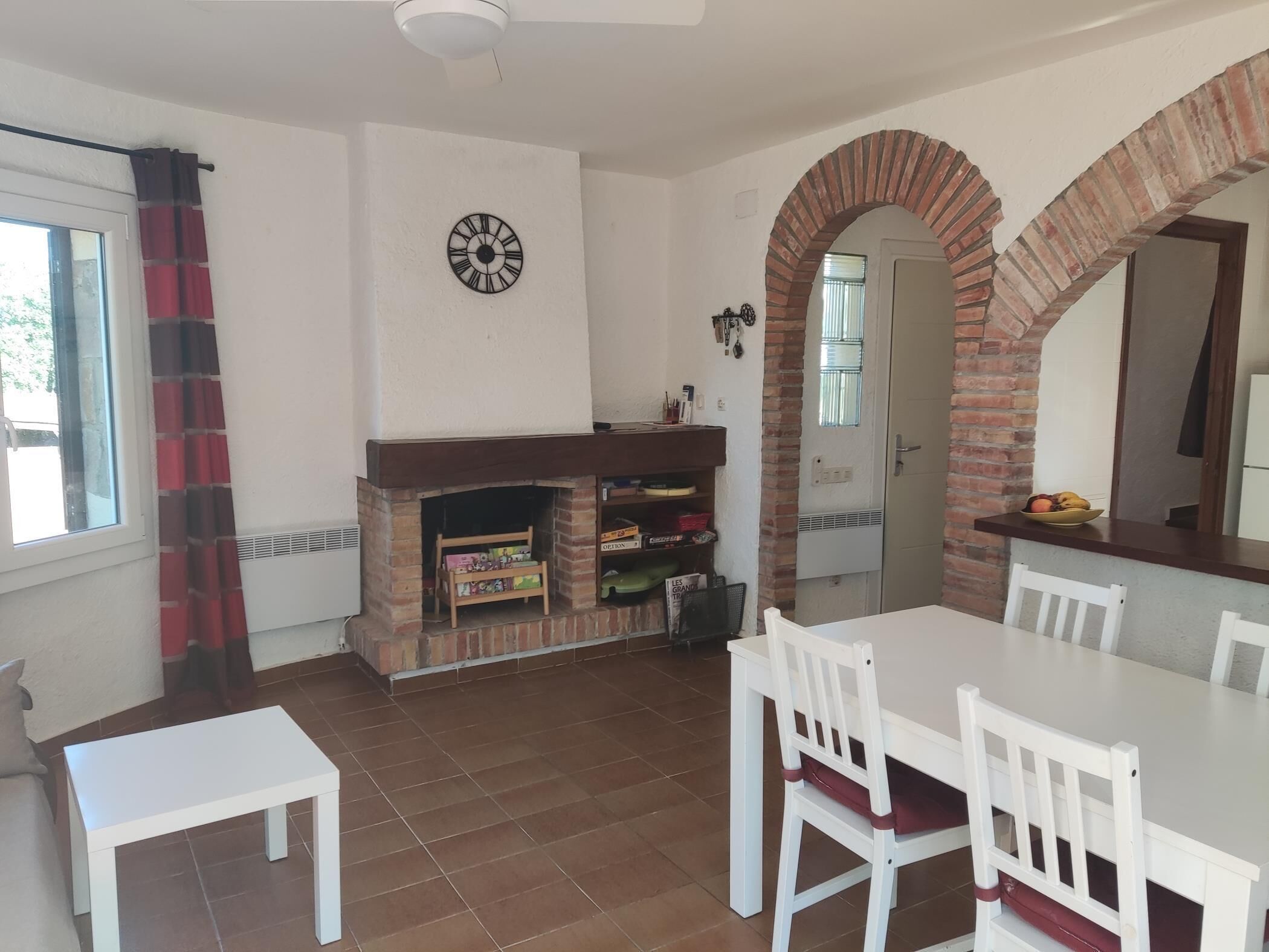 Un comedor con chimenea de ladrillo, sillas blancas, una mesa blanca y un reloj en la pared.