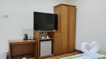 A small room with a wooden desk, a television, a mini-fridge, a cabinet, a trash bin, and a pair of slippers.