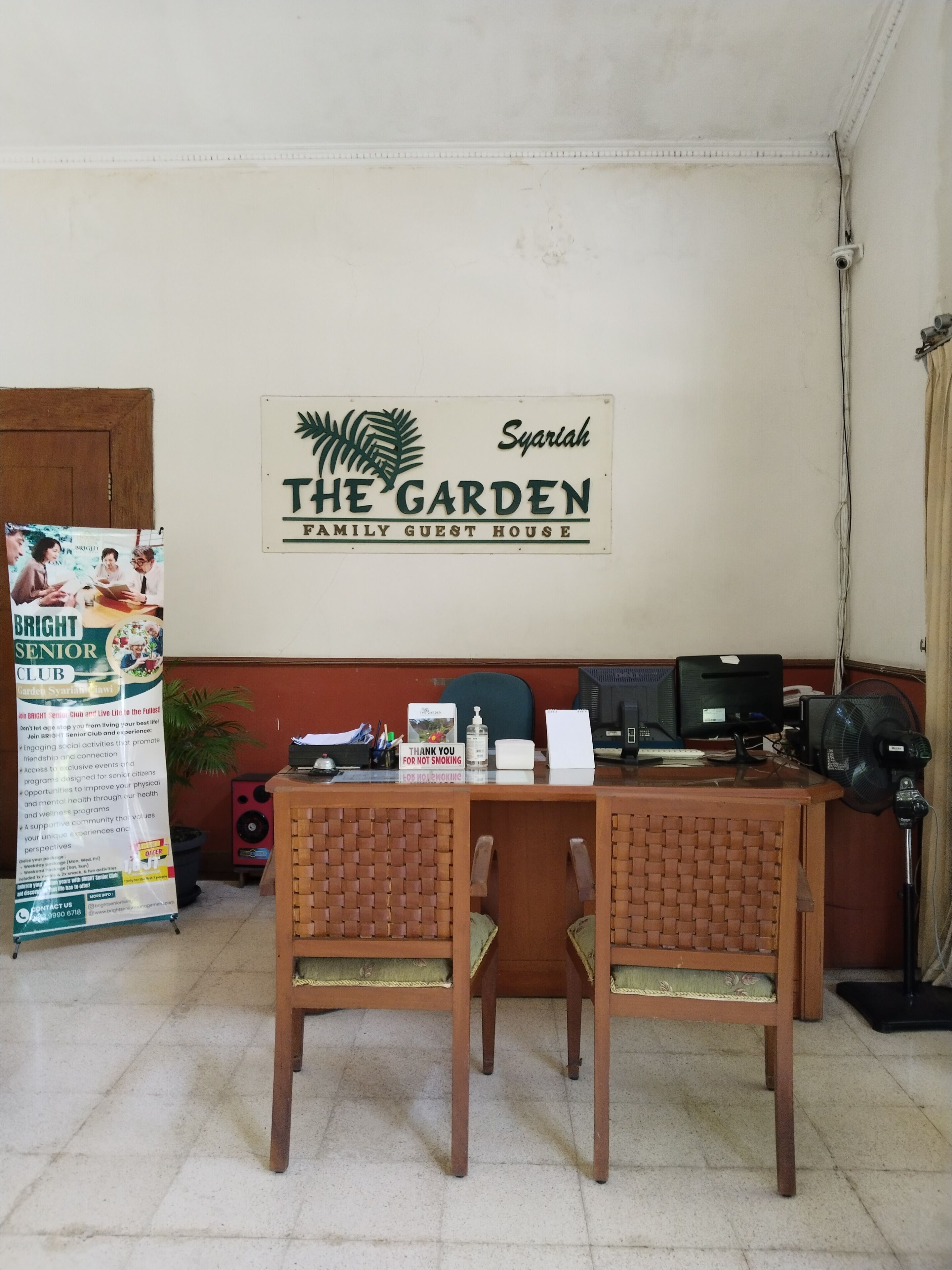 A reception area with a sign for 'The Garden Family Guest House' and a 'Bright Senior Club' poster.