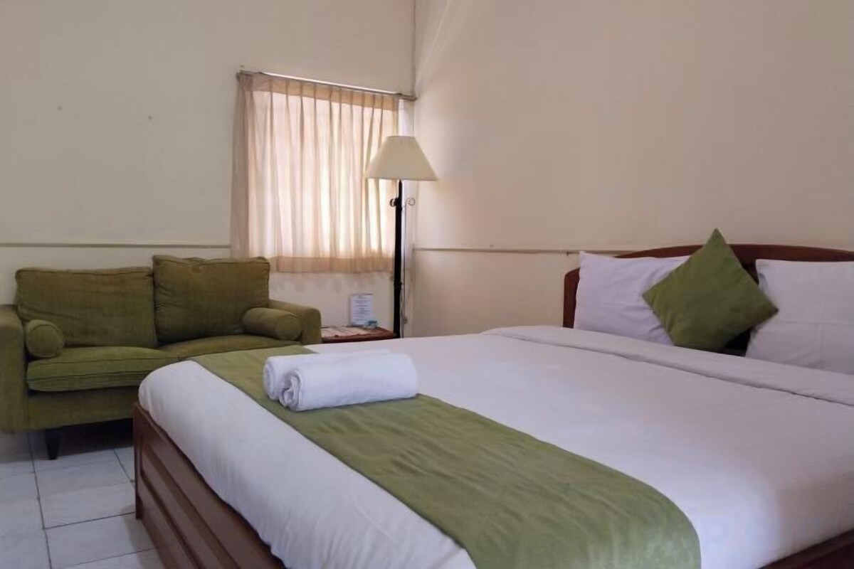 A hotel room with a bed, a green sofa, a nightstand, and a lamp.