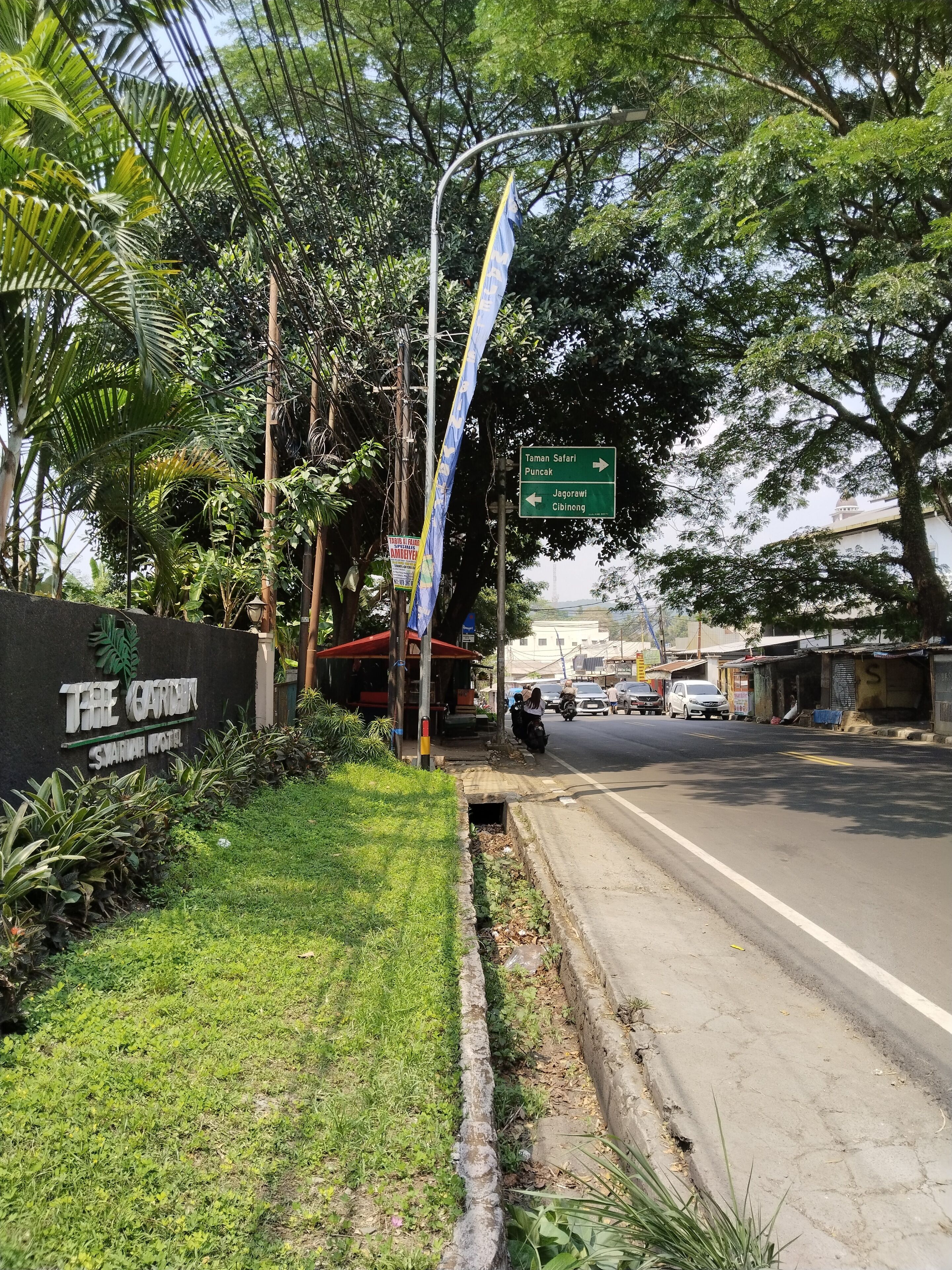 Straatbeeld met een bord voor 'The Garden Swam Hotel' en pijlen naar 'Taman Safari Puncak' en 'Jagorawi Cibinong'.