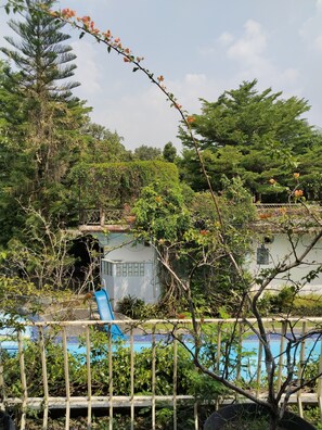 A pool area with a wooden fence, a blue slide, and lush greenery. - The Garden Family Guest House powered by Cocotel. (Ciawi)