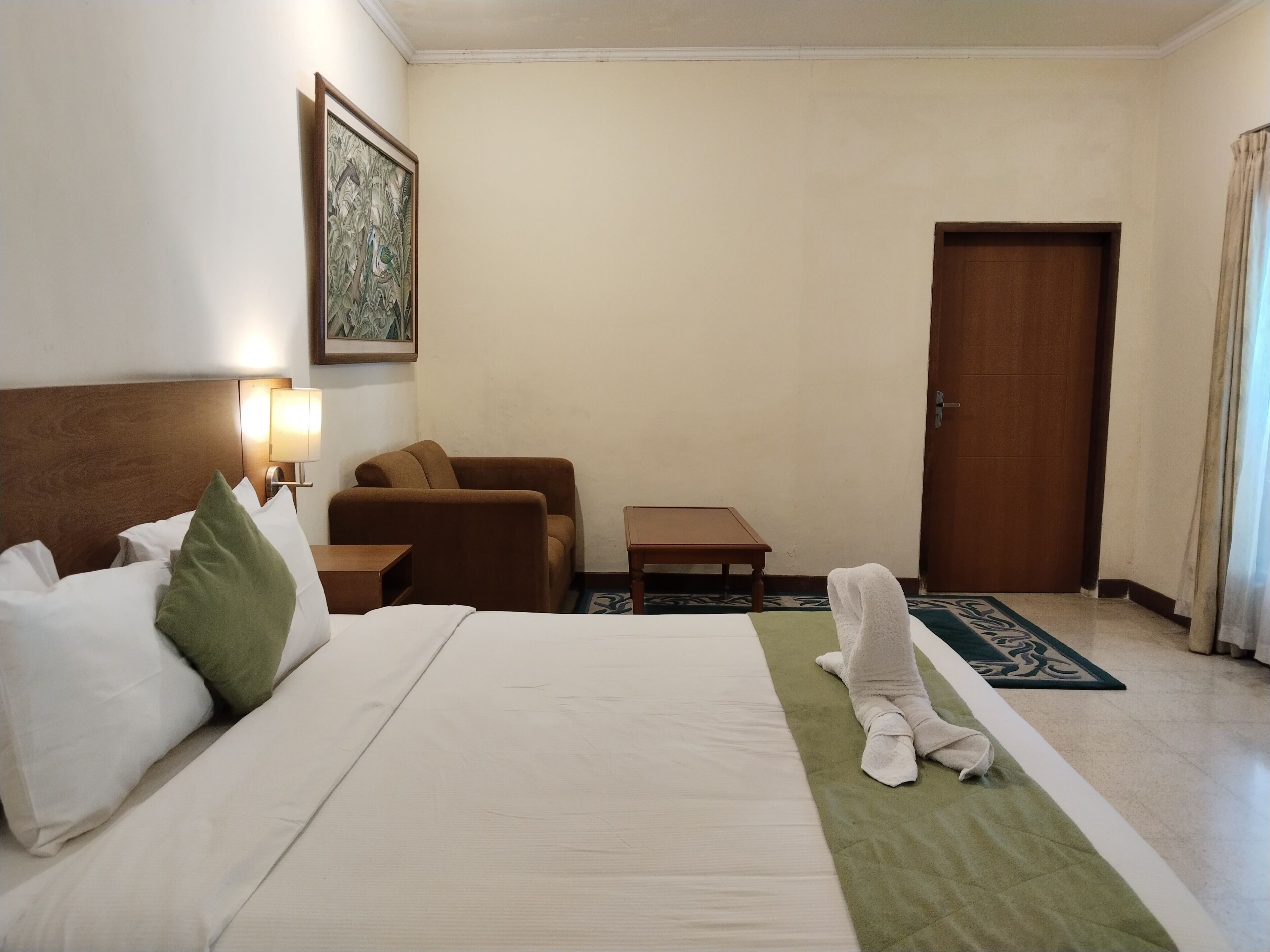 A hotel room with a bed, a sofa, a small table, a lamp, and a door.