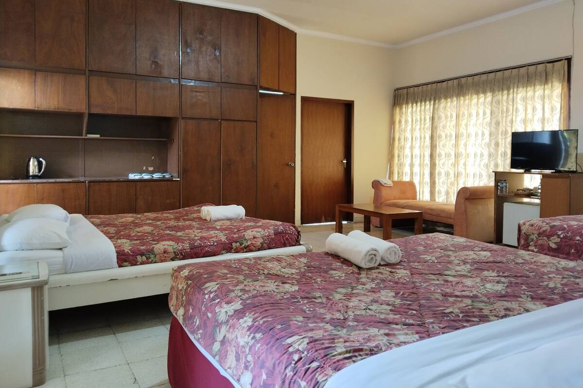 A hotel room with two beds, a wooden wardrobe, a television, and a small table.
