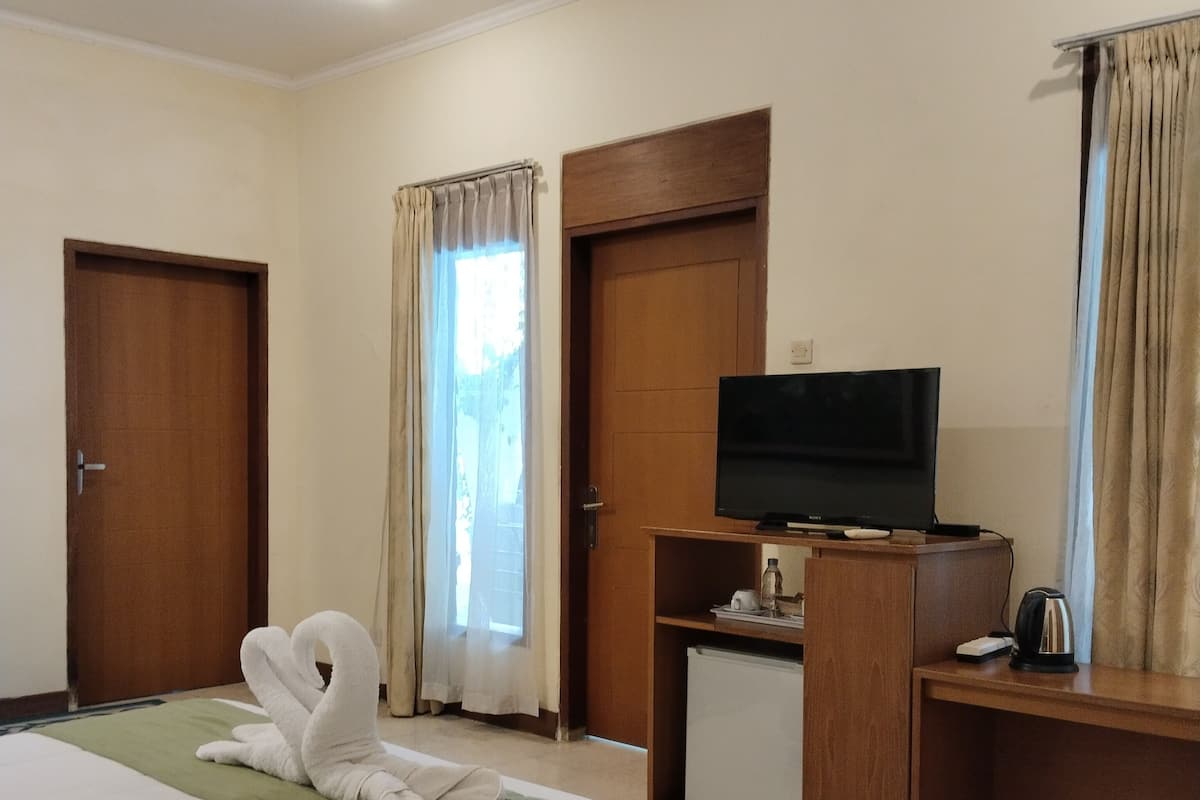 A hotel room with a bed, a television on a wooden stand, a desk with a kettle, and a window with curtains.