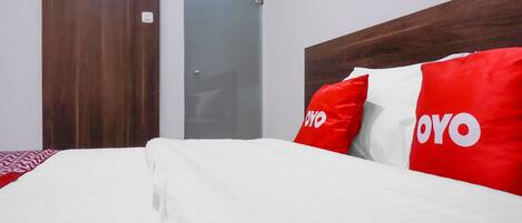 A hotel room with a wooden headboard, a bed with white bedding, and red and white pillows with the word "OYO" on them.