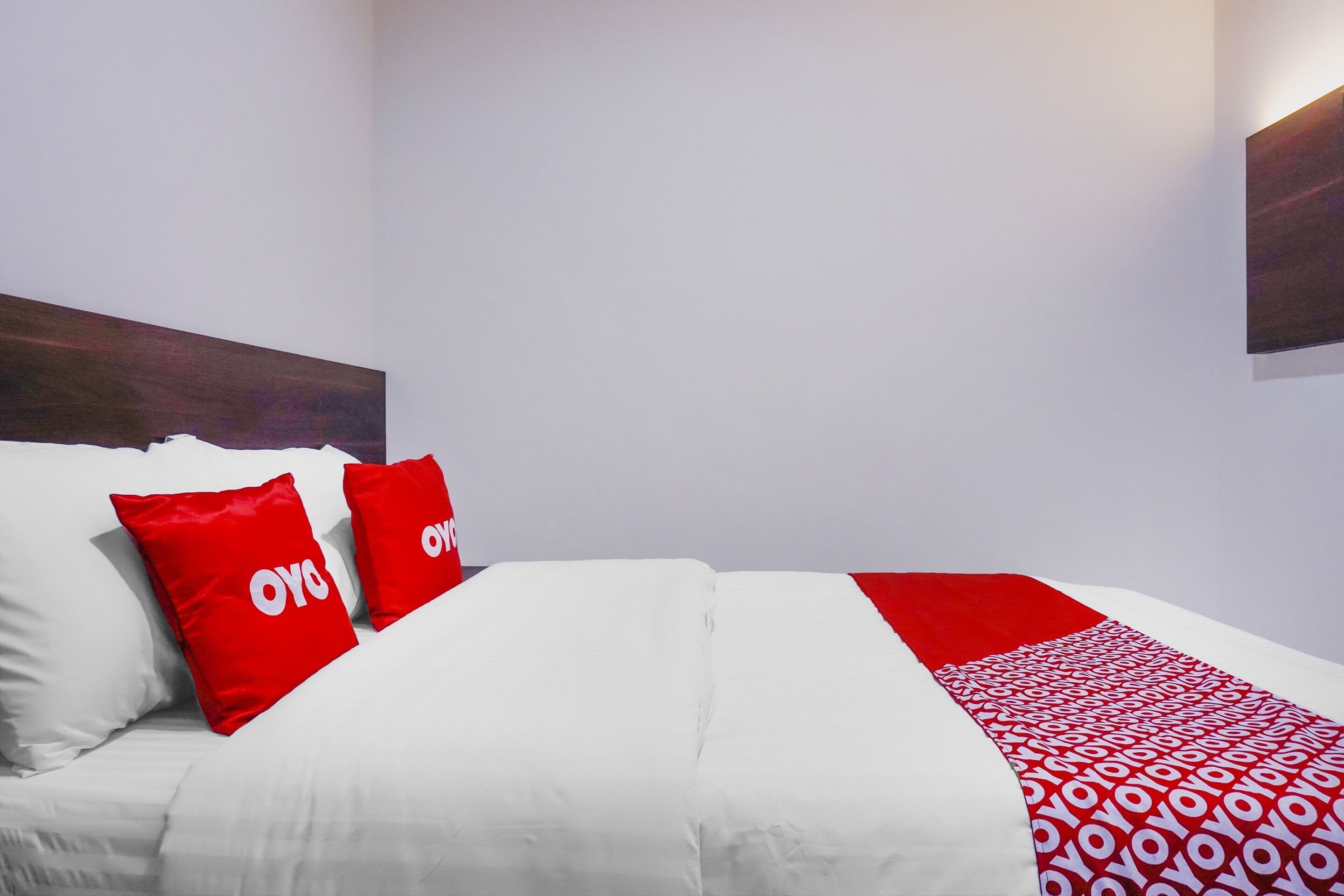 A neatly made bed with white bedding and red pillows, a red and white patterned throw, and a dark wooden headboard.