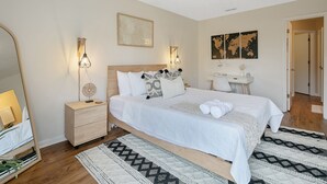 A neatly arranged bedroom with a large bed, bedside tables, a mirror, and wall-mounted lights.