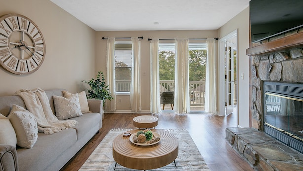 A living room with a beige sofa, a wooden coffee table, a large wall clock, and a stone fireplace.