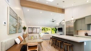 Una cucina moderna con isola centrale, sgabelli da bar e una zona relax con una panca e sedie.