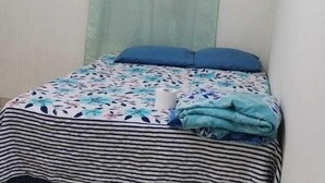 A small, single-bed room with a striped bedspread, a light green curtain, and a blue pillow. - Hostal Maya Land (Santa Cruz del Quiché)