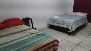 A small, simple room with two beds, one with a striped blanket and the other with a quilt. There is a chair and a red pillow on the left bed. - Hostal Maya Land (Santa Cruz del Quiché)
