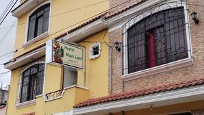 A two-story building with a yellow facade, a sign for 'Hostal Maya Land', and closed garage doors. - Hostal Maya Land (Santa Cruz del Quiché)
