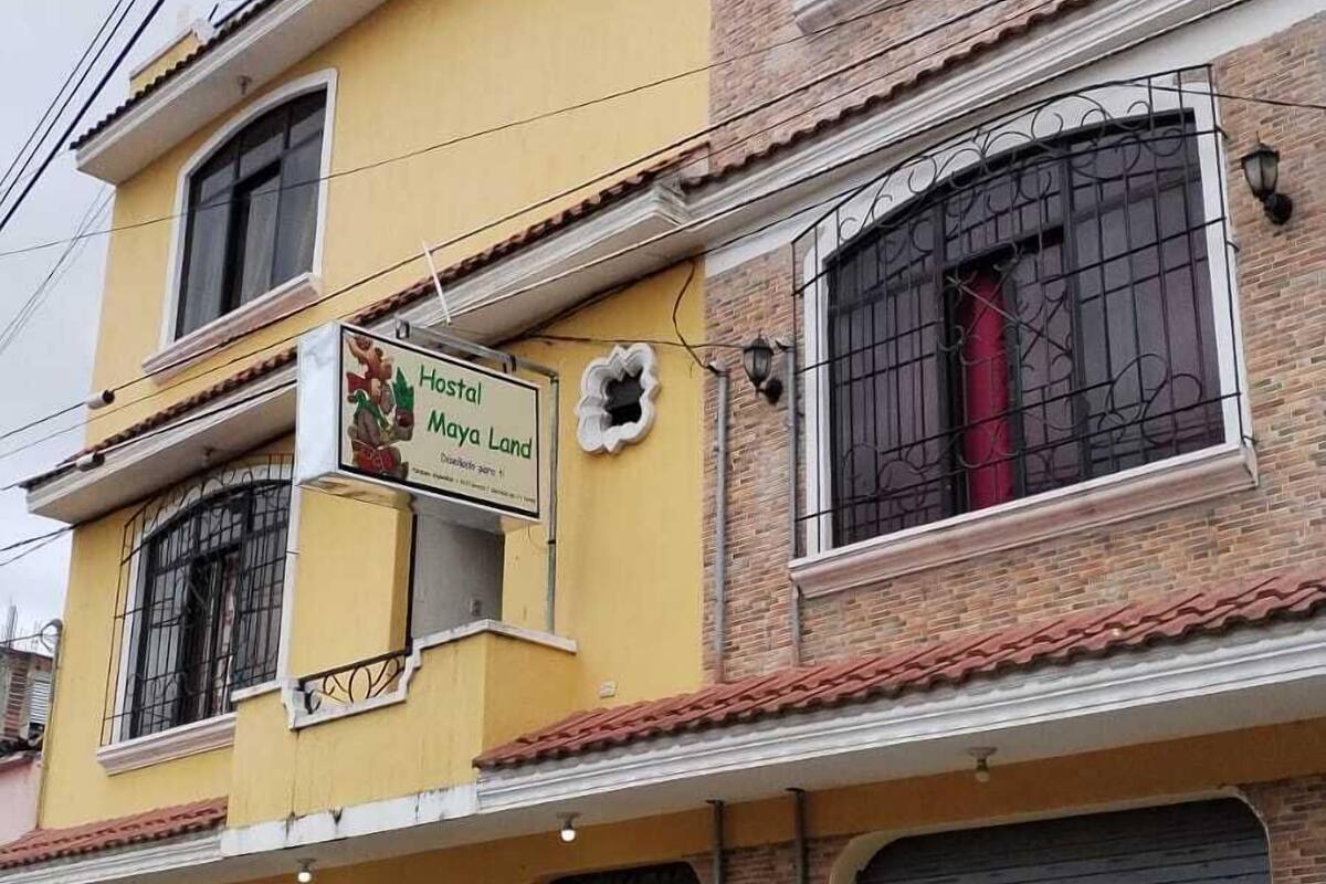 A two-story building with a yellow facade, a sign for 'Hostal Maya Land', and closed garage doors.