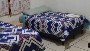A room with two beds, each with patterned bedding, a small table, and a framed picture on the wall. - Hostal Maya Land (Santa Cruz del Quiché)