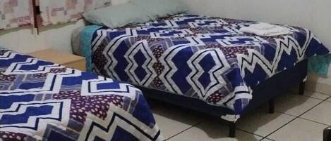A room with two beds, each with patterned bedding, a small table, and a framed picture on the wall.