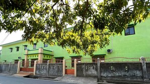 A green building with a gated entrance, multiple windows, and a concrete wall.