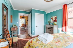 A bedroom with teal walls, a bed with a floral bedspread, a wooden chair, a dresser, and a window with red curtains.