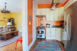 Cocina compacta con alacenas blancas, refrigerador de acero inoxidable y una silla roja.