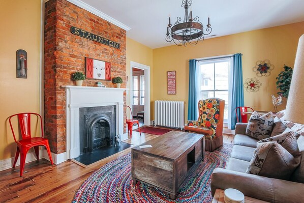 A living room with a brick fireplace, a sofa, a coffee table, and a colorful rug.