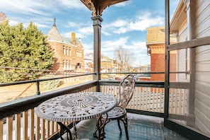 A balcony with a wrought iron table and chairs, overlooking a historic building and a wooden fence.