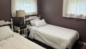 Une chambre avec deux lits simples, une table de chevet avec une lampe et une fenêtre avec des rideaux légers.