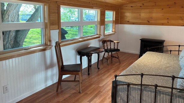 Une pièce avec un plafond et des murs en bois, de grandes fenêtres, un lit, une table et deux chaises.