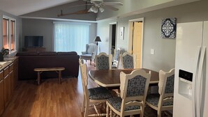 Un vaste espace de vie comprenant un ventilateur de plafond, une table à manger avec des chaises, un canapé et un téléviseur.
