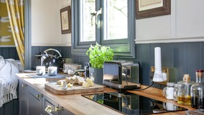 A kitchen with a toaster, a cutting board with cheese, a plant, and a window with curtains.