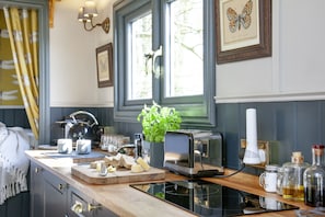 A kitchen with a toaster, a cutting board with cheese, a plant, and a window with curtains.
