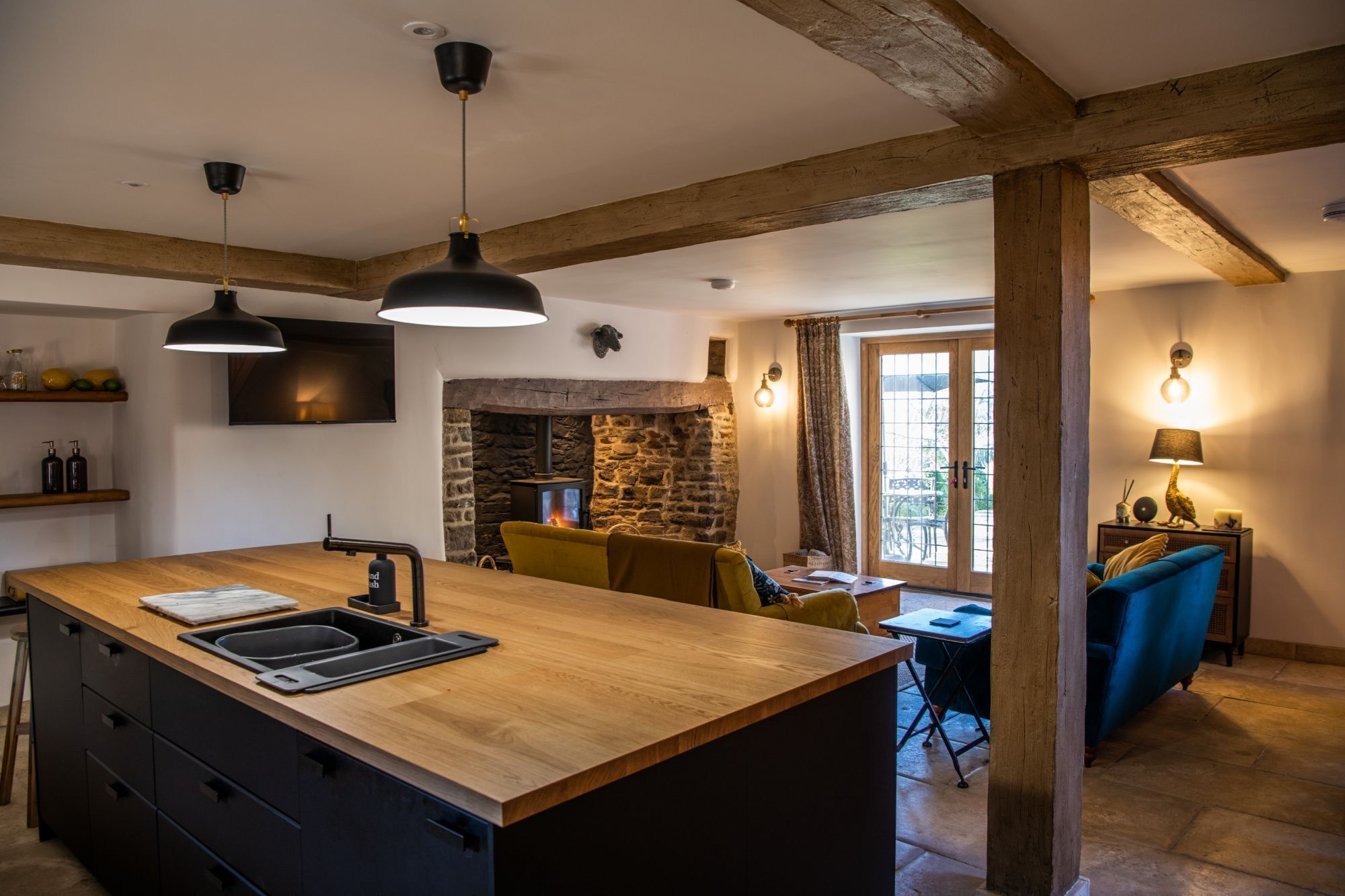 A kitchen with a central island, wooden beams, a stone fireplace, and a dining area with a blue sofa.