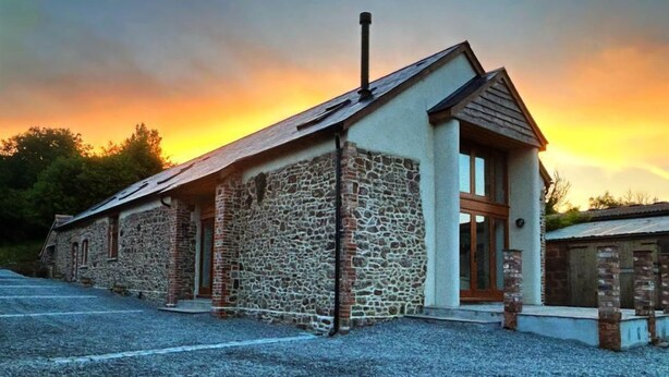 Un edificio in pietra con tetto spiovente e camino, caratterizzato da un'ampia porta vetrata e un piccolo portico.
