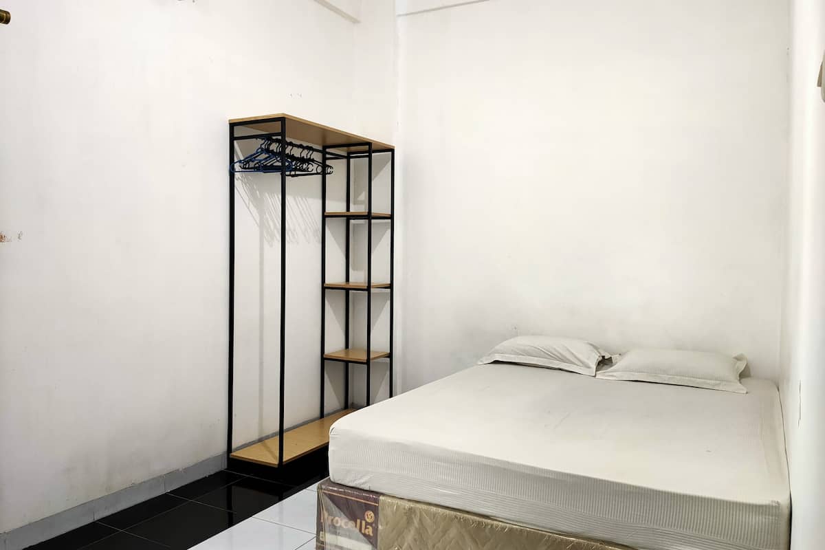 A small, clean room with a bed, a metal wardrobe, and a tiled floor.