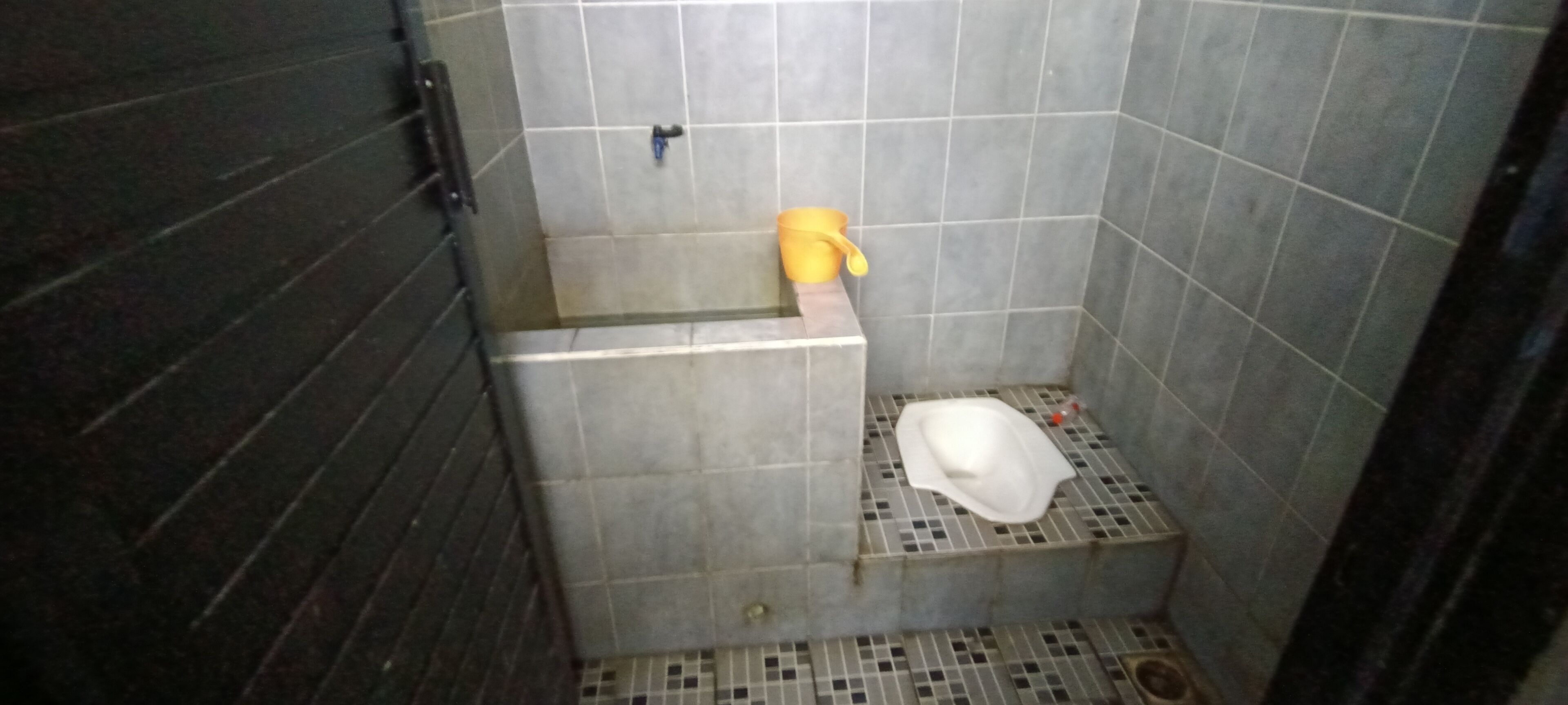 A small, tiled bathroom with a shower area, a toilet, and a yellow bucket.