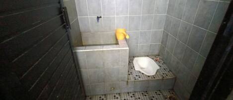 Et lille badeværelse med fliser, en bruseniche, toilet og en gul spand.
