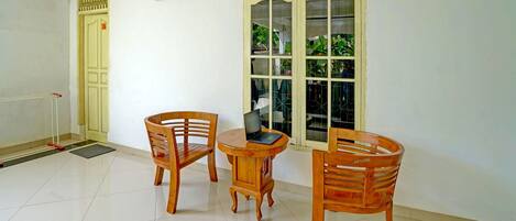 A room with a wooden table and two chairs, a clock on the wall, and a window with a view of greenery.