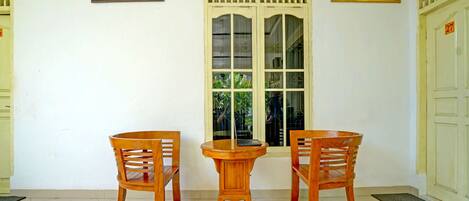 A room with a wooden table and two chairs, a window with a clock, and two framed artworks on the wall.