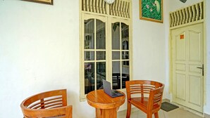Ein Zimmer mit einem Holztisch und zwei Stühlen, einem Fenster mit dekorativen Fensterläden und einer Tür mit einer Nummer.'