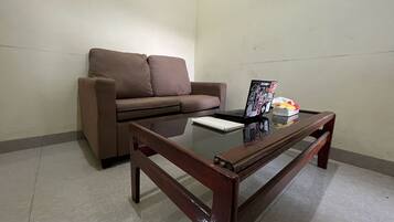 A living room with a brown sofa, a glass coffee table, and a laptop.
